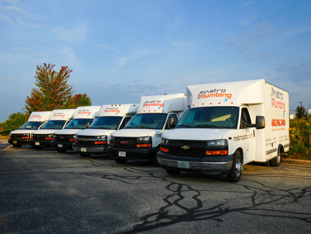 6 White Metro Plumbing trucks parked next to each other with logo and contact information on the side. Shows website as: metropdc.com and the phone number as 606.906.7400