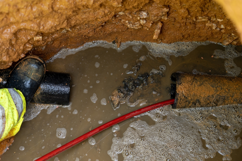 Broken sewer pipe and water in the group with a worker inserting a red wire through it